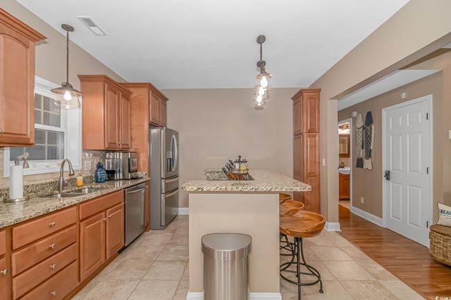 Kitchen featuring appliances with stainless steel finishes, a center island, a kitchen breakfast bar, light stone countertops, and hanging light fixtures | Image 8