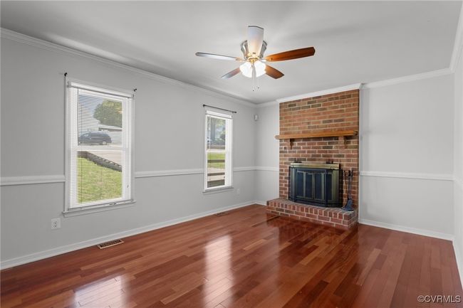 Unfurnished living room featuring hardwood / wood-style floors, visible vents, baseboards, a brick fireplace, and ceiling fan | Image 8