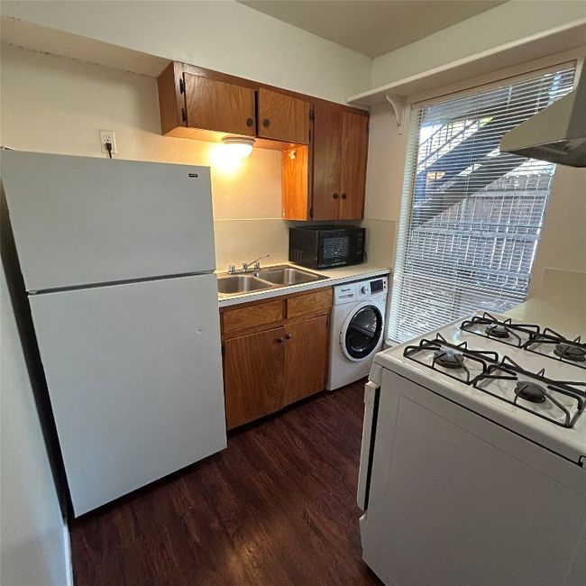 Kitchen with dark wood-type flooring, washer / dryer, range hood, white appliances, and a sink | Image 11