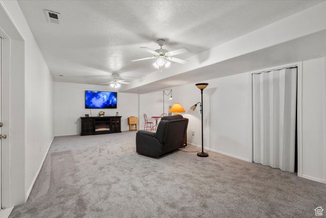 Living area featuring a ceiling fan, carpet, baseboards, a textured ceiling, and a warm lit fireplace | Image 25