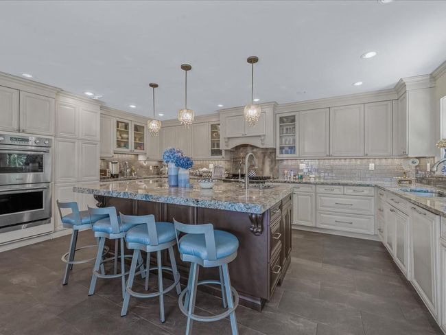 Kitchen featuring stainless steel double oven, a sink, an island with sink, backsplash, and glass insert cabinets | Image 8