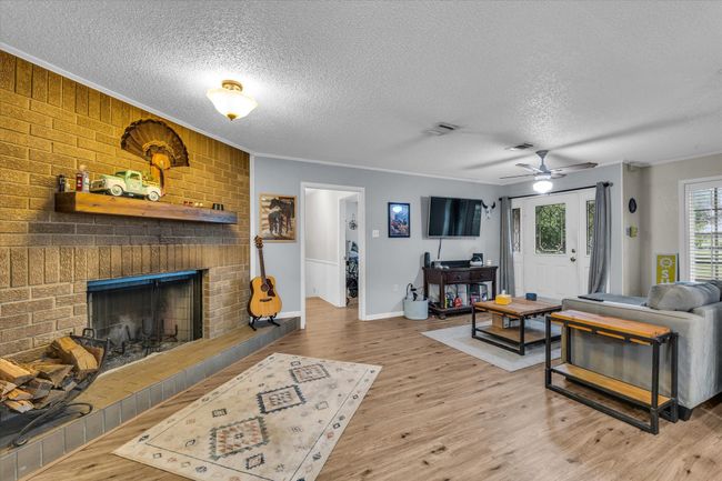 Living area featuring a textured ceiling, wood finished floors, ornamental molding, a brick fireplace, and a ceiling fan | Image 19
