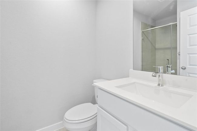 Secondary bath features tile flooring, walk-in shower with tile surround, stained wood cabinets, beautiful light countertops, mirror, sleek fixtures, and modern finishes. This secondary bathroom has private access to a secondary bedroom. | Image 15