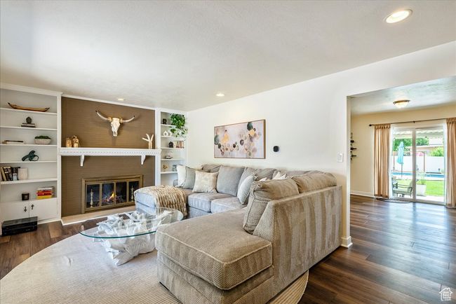 Living area with dark wood-type flooring, a glass covered fireplace, and recessed lighting | Image 10
