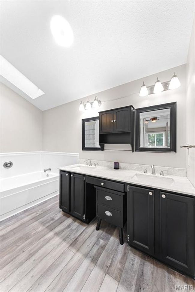 Full bathroom featuring double vanity, a skylight, a jetted tub, and separate shower. | Image 12
