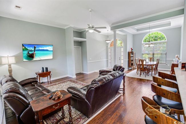 Living room featuring dark wood-style floors, a chandelier, a ceiling fan, crown molding, and decorative columns | Image 11