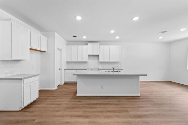 This light and bright kitchen features a large quartz island, white cabinets, a large sink overlooking your family room, recessed lighting, and beautiful backsplash. | Image 8