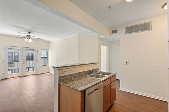Kitchen featuring dark wood finished floors, stainless steel dishwasher, brown cabinets, a kitchen island with sink, and open floor plan | Image 9