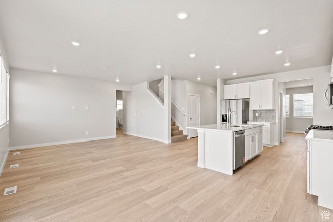 Kitchen with appliances with stainless steel finishes, white cabinetry, light wood-style floors, an island with sink, and light countertops | Image 6