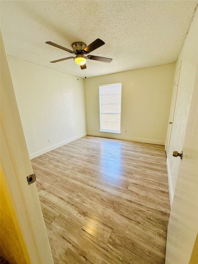 Empty room with a textured ceiling, light wood-style floors, a ceiling fan, and baseboards | Image 11