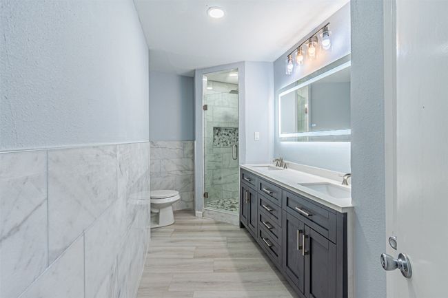Bathroom with tile walls, vanity, toilet, and walk in shower | Image 36