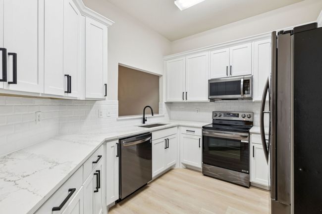 Kitchen featuring appliances with stainless steel finishes, white cabinetry, backsplash, and light wood finished floors | Image 6