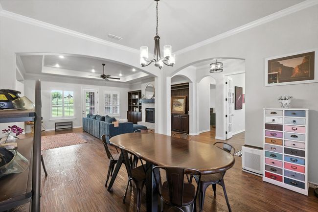Dining space featuring arched walkways, a ceiling fan, dark wood-type flooring, crown molding, and a fireplace | Image 8