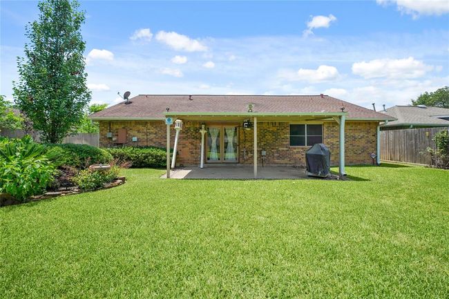Photo shows the backyard of a brick house featuring a covered patio area. The yard is spacious and well-maintained, with green grass and surrounding landscaping, offering a private and inviting outdoor space for relaxing or entertaining. | Image 25