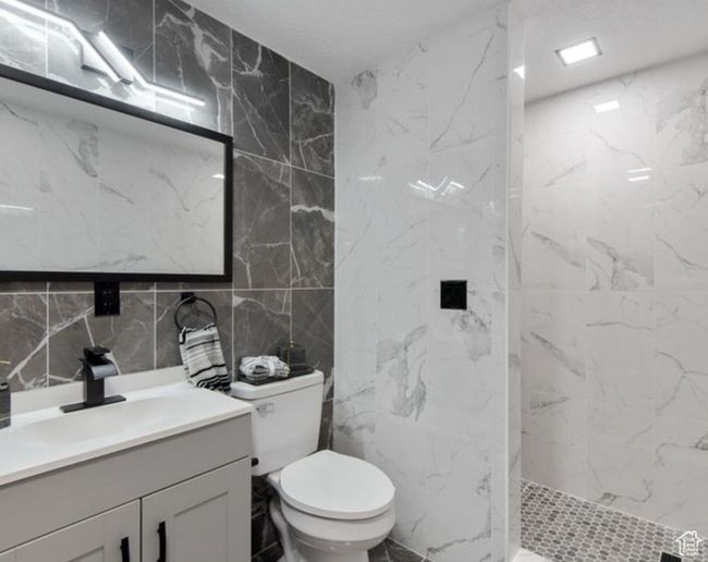 Bathroom featuring tile walls, vanity, a marble finish shower, toilet, and decorative backsplash | Image 16