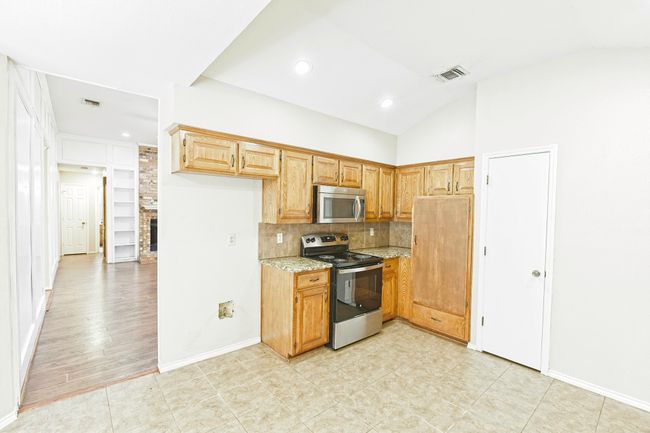 Kitchen with appliances with stainless steel finishes, light stone counters, decorative backsplash, lofted ceiling, and recessed lighting | Image 12