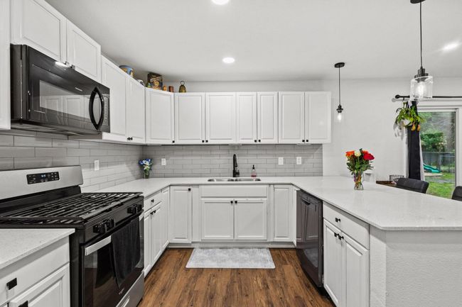 Kitchen with black microwave, stainless steel range with gas cooktop, a sink, a peninsula, and dark wood finished floors | Image 9