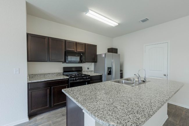 Kitchen featuring black appliances, a sink, light wood-style floors, dark brown cabinetry, and a center island with sink | Image 8