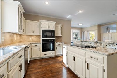 Kitchen with ornamental molding, white cabinetry, dark hardwood flooring, and black appliances | Image 1