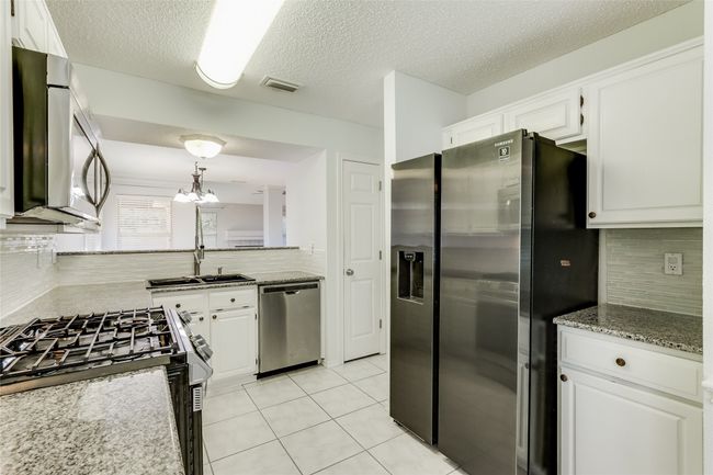 Kitchen featuring light tile patterned floors, a sink, backsplash, stainless steel appliances, and white cabinets | Image 15
