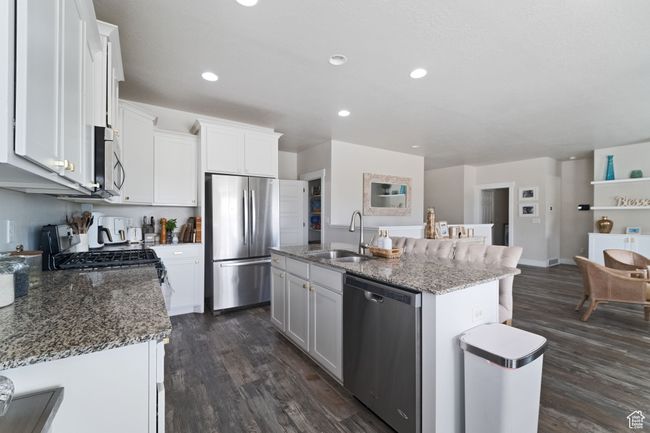 Kitchen featuring stainless steel appliances, white cabinets, dark wood-style flooring, a sink, and stone countertops | Image 4