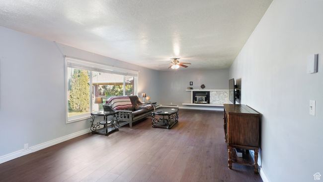 Living area with ceiling fan, a glass covered fireplace, a textured ceiling, dark wood-type flooring, and baseboards | Image 11