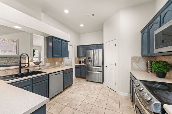 Kitchen with appliances with stainless steel finishes, a sink, light countertops, backsplash, and light tile patterned floors | Image 10