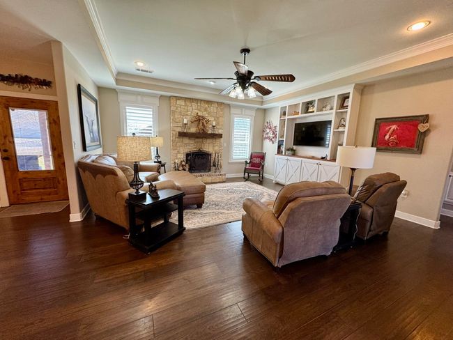 Living room with a ceiling fan, a fireplace, dark wood finished floors, baseboards, and ornamental molding | Image 7