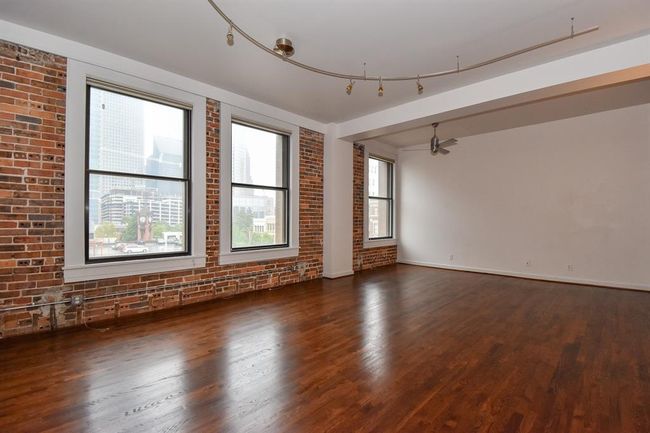 Alternate view of the living area highlights the open layout and beautiful hardwood floors, with expansive windows framing vibrant downtown views and flooding the space with natural light. | Image 11