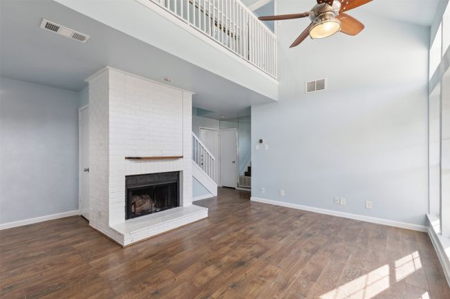 Unfurnished living room with a brick fireplace, wood finished floors, visible vents, and baseboards | Image 5