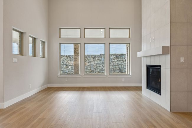 Unfurnished living room with light wood finished floors, a tile fireplace, and a towering ceiling | Image 13