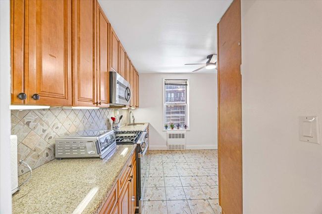 Kitchen with appliances with stainless steel finishes, radiator heating unit, ceiling fan, decorative backsplash, and light stone counters | Image 5