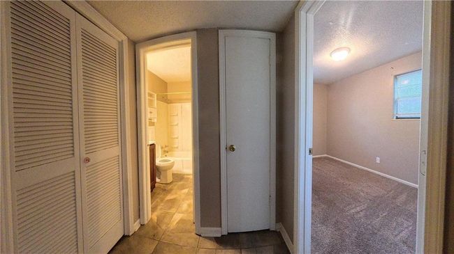 Hall with a textured ceiling, tile patterned flooring, and carpet flooring | Image 6