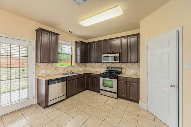 Kitchen with appliances with stainless steel finishes, dark brown cabinetry, decorative backsplash, and light tile patterned floors | Image 10