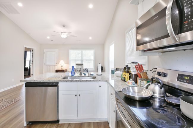 Kitchen featuring stainless steel appliances, vaulted ceiling, a ceiling fan, white cabinets, and light wood-type flooring | Image 10