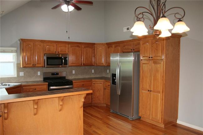 Kitchen with appliances with stainless steel finishes, light wood finished floors, high vaulted ceiling, a kitchen breakfast bar, and decorative backsplash | Image 5