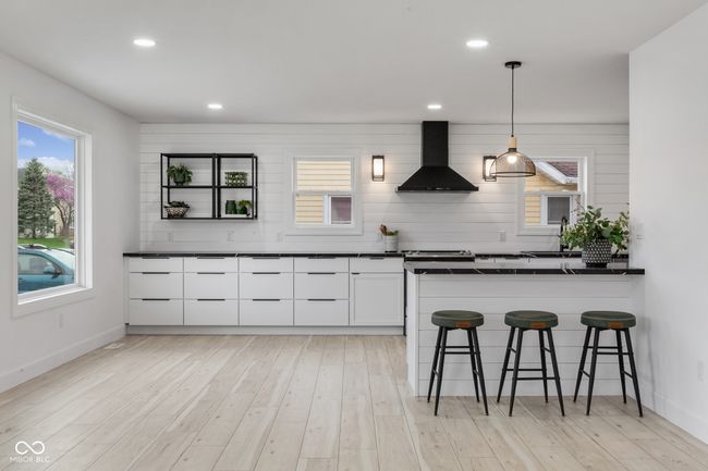 kitchen with white cabinets, wall chimney range hood, dark countertops, a kitchen breakfast bar, and light wood finished floors | Image 18