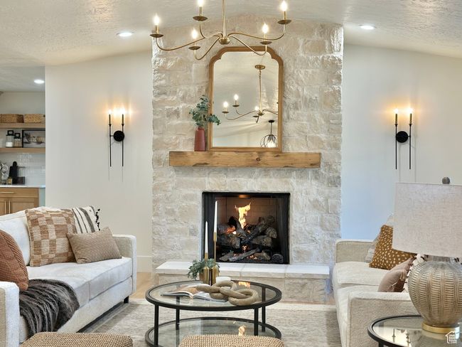 Living room with a chandelier, a stone fireplace, a textured ceiling, and wood finished floors | Image 5