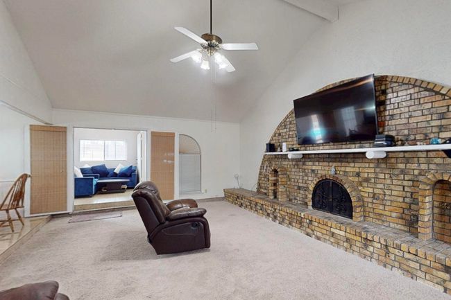 Living area with high vaulted ceiling, carpet, a brick fireplace, a ceiling fan, and beam ceiling | Image 8