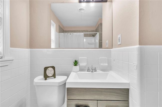 Full bathroom with a wainscoted wall, a shower with curtain, toilet, tile walls, and vanity | Image 33