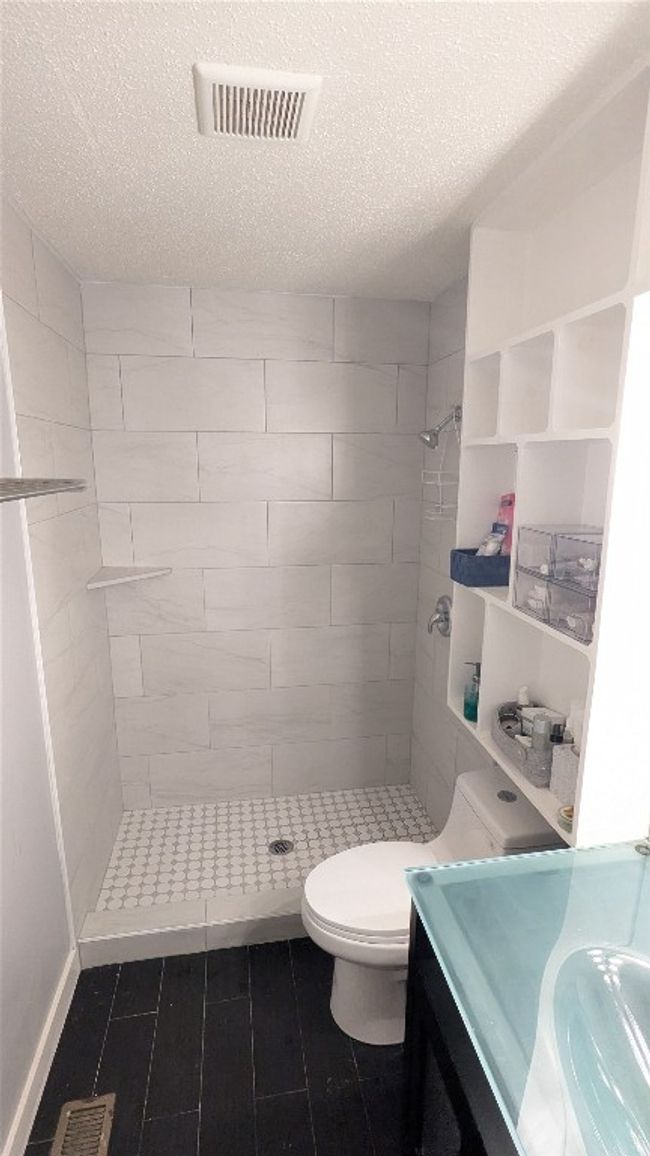 Bathroom with tiled shower, a textured ceiling, vanity, tile patterned flooring, and toilet | Image 18