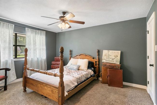 Cozy bedroom with a rustic wooden bed and vintage decor. Features a ceiling fan, carpeted floor, and a window with light curtains, offering a warm, inviting atmosphere. | Image 37