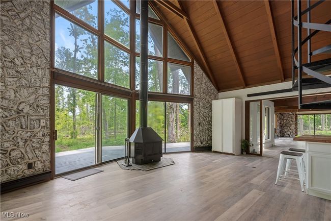 Unfurnished living room featuring high vaulted ceiling, a wood stove, wood ceiling with exposed beams, healthy amount of natural light, and wood finished floors | Image 11