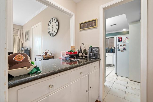 This convenient wet bar is perfect for entertaining, featuring a sleek granite countertop, built-in sink, and ample cabinet storage. Located between the main living areas and kitchen, it provides the ideal space for mixing drinks or serving guests with ease. | Image 17