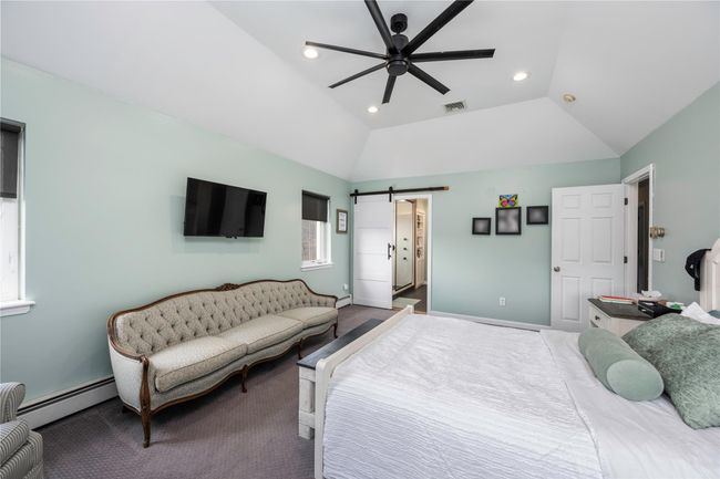 Bedroom featuring vaulted ceiling, a raised ceiling, dark carpet, ceiling fan, and a tiled fireplace | Image 17