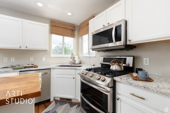 Kitchen with stainless steel appliances, white cabinetry, recessed lighting, dark wood-style floors, and light stone counters | Image 8