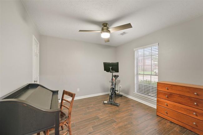 There's a versatile first-floor bedroom with wood-look tile flooring, a modern ceiling fan, and a front-facing window—ideal as a guest room, home office, or fitness space. | Image 15