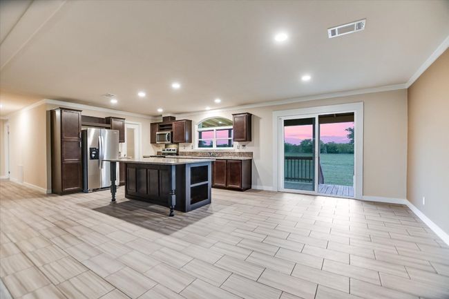 Kitchen featuring appliances with stainless steel finishes, crown molding, dark brown cabinetry, light countertops, and a center island | Image 10