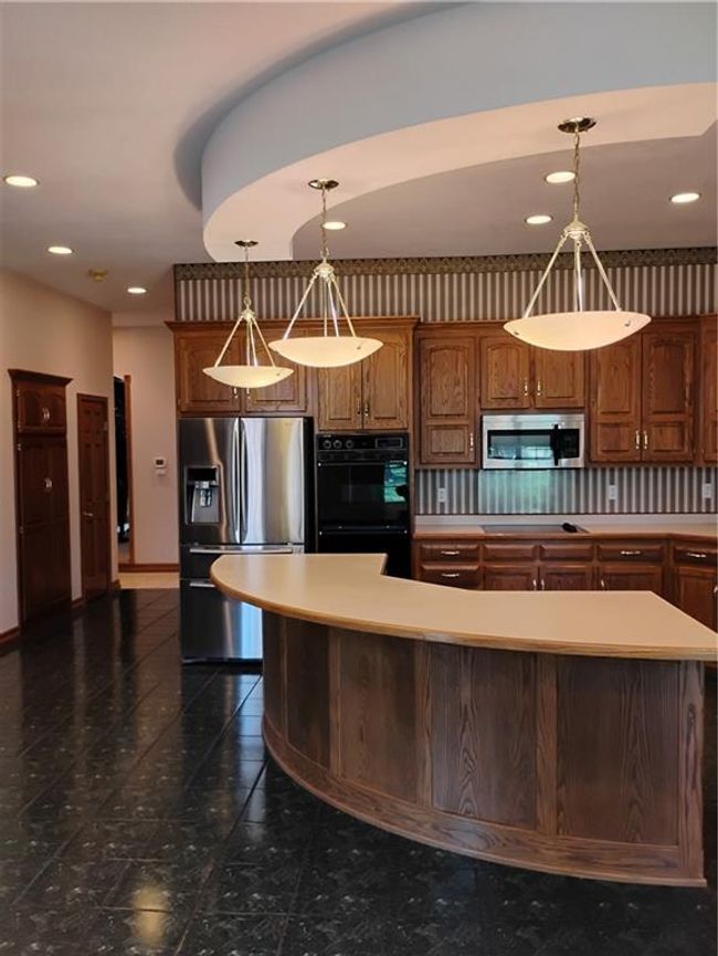 Kitchen with light countertops, dobule oven black, fridge, and brown cabinetry, microwave | Image 31