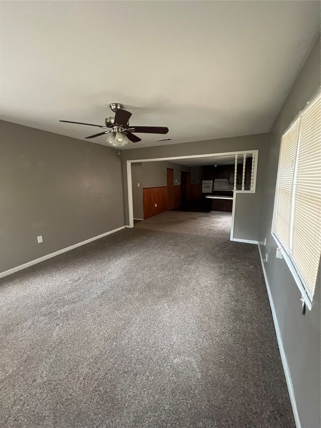 Unfurnished living room featuring ceiling fan, dark colored carpet, and baseboards | Image 4
